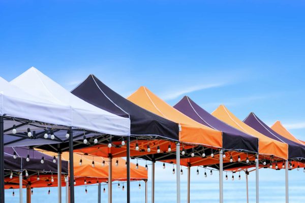 Many foldable canopy tents with hanging LED light bulbs decoration for outdoors event on the beach